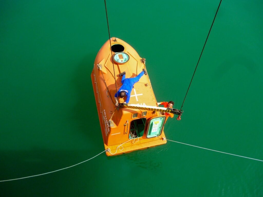 Aerial view of an orange rescue capsule with two people over green water.